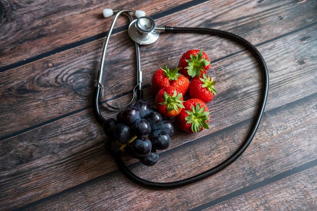 Fraises écossaises rouges et raisins noirs avec stéthoscope sur le dessus de la table en bois. Conceptuel alimentaire médical et sain.