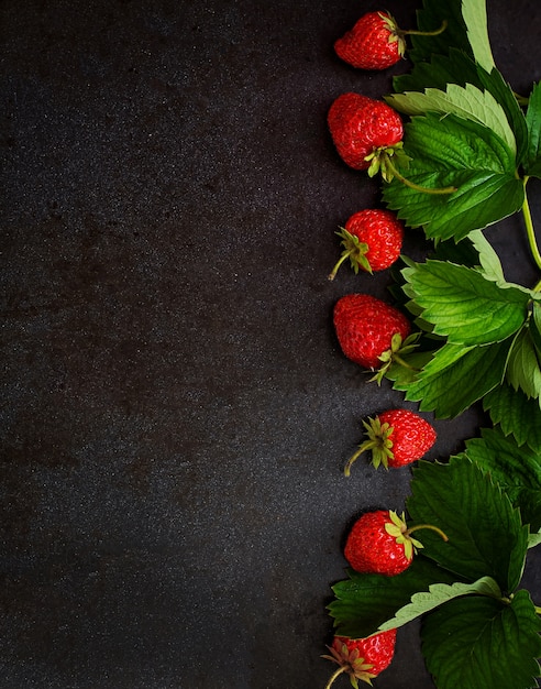 Fraises mûres et feuilles sur fond noir. Vue de dessus