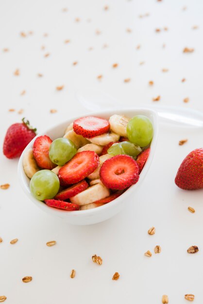 Des fraises; raisins et des tranches de banane dans un bol tartinés d&#39;avoine sur fond blanc