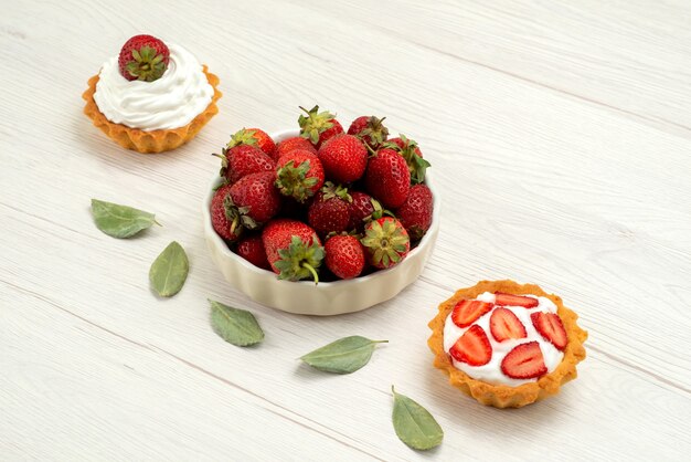 Fraises rouges fraîches moelleuses et délicieuses baies à l'intérieur de la plaque avec des gâteaux sur un bureau léger