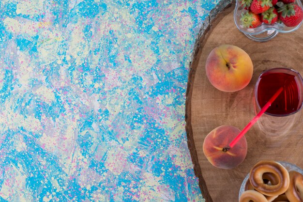 Fraises rouges et pêches avec un verre de jus et biscuits sur un plateau en bois