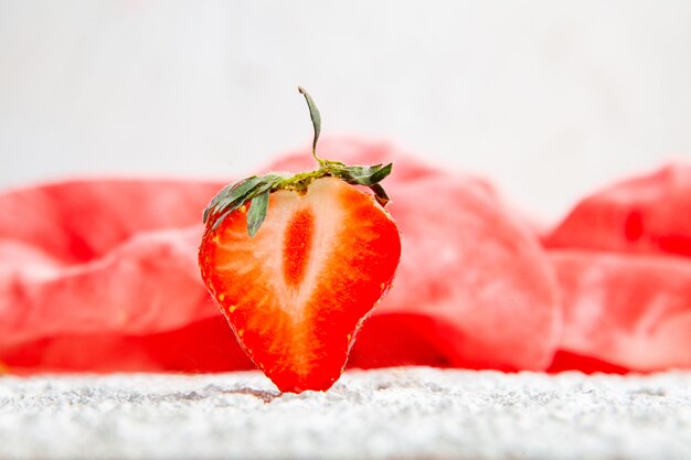 Fraises sur un tissu rouge et fond texturé blanc. vue de côté.