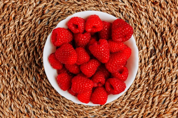 Framboises dans un bol vue de dessus sur un fond texturé de dessous de plat