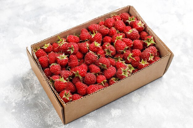 Framboises douces mûres en boîte sur du béton gris. Gros plan, vue de dessus