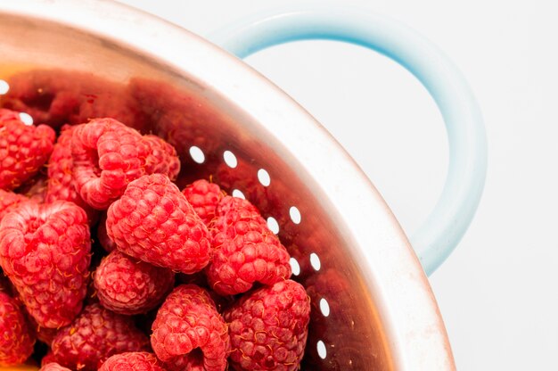 Framboises rouges dans une passoire en acier inoxydable sur fond blanc