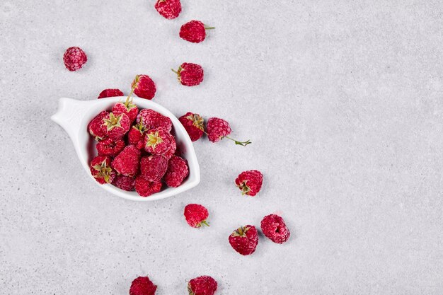 Framboises rouges fraîches dans un bol blanc sur une surface blanche. Vue de dessus.