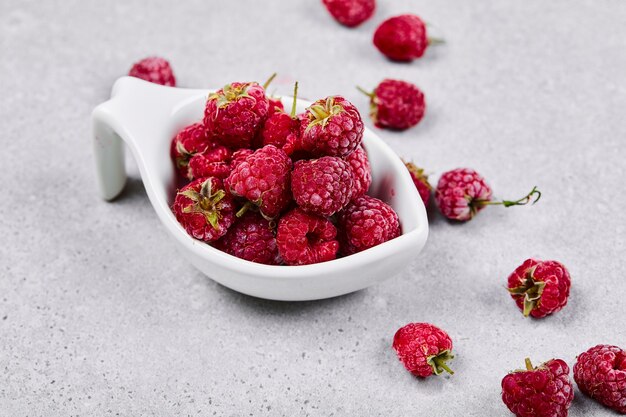 Framboises rouges fraîches dans un bol blanc sur une surface blanche.