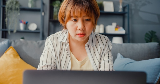 Freelance Asian lady casual wear à l'aide d'un ordinateur portable apprentissage en ligne dans le salon à la maison