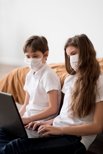 Frères et sœurs avec masque à l'aide d'un ordinateur portable