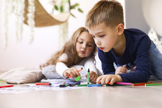 Les frères et sœurs tiennent des crayons brillants et dessinent sur le sol