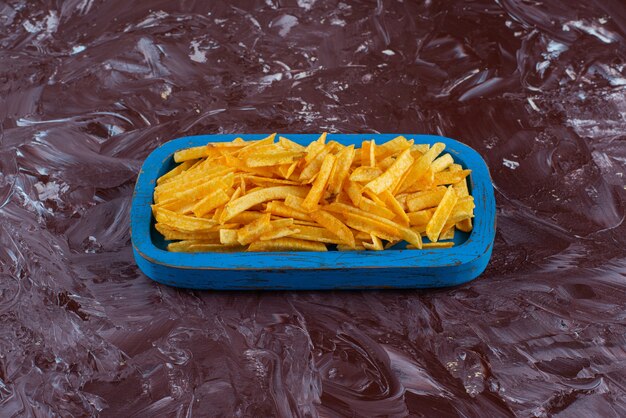 Frites de pommes de terre savoureuses dans une assiette en bois sur la surface en marbre