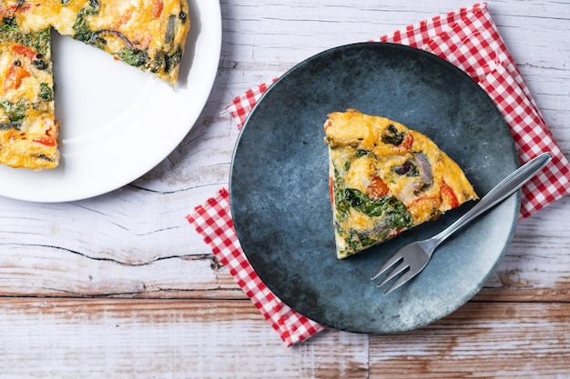 Photo gratuite frittata italienne à base de tomates épinards, oignons et poivrons sur table en bois blanc