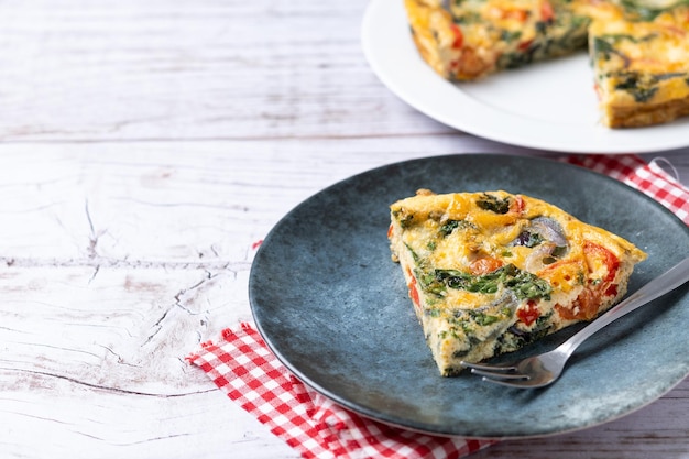 Frittata italienne à base de tomates épinards, oignons et poivrons sur table en bois blanc