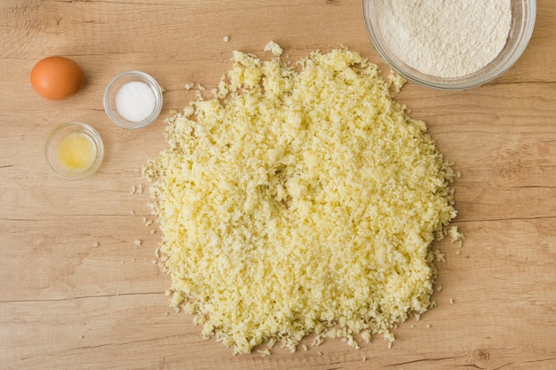 Fromage râpé; sel; Oeuf; farine pour préparer des gnocchi italiens sur un bureau en bois