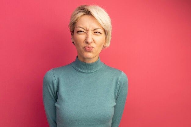 Fronçant les sourcils jeune femme blonde regardant les lèvres pincées avant isolées sur le mur rose avec espace de copie