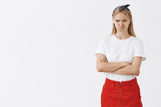 Fronçant les sourcils jeune fille blonde posant contre le mur blanc