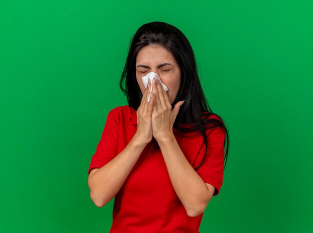 Fronçant les sourcils jeune fille malade de race blanche essuyant le nez avec une serviette avec les yeux fermés isolé sur un mur vert avec espace de copie