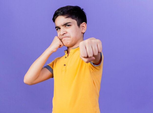 Fronçant les sourcils jeune garçon de race blanche touchant le visage avec le poing étirant le poing vers isolé sur mur violet avec espace de copie