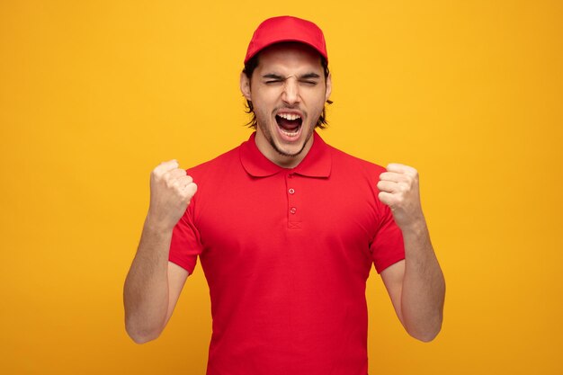 fronçant les sourcils jeune livreur portant l'uniforme et la casquette montrant oui geste criant les yeux fermés isolé sur fond jaune