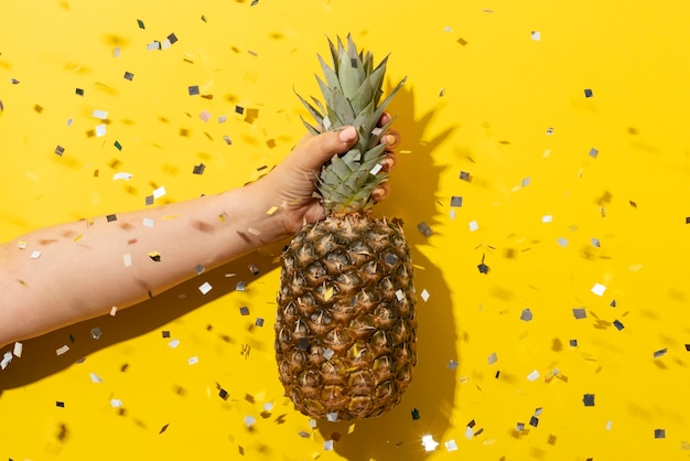 Fruit d'ananas tenu à la main avec des confettis