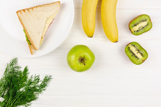 Fruits avec une assiette avec un sandwich sur une table blanche