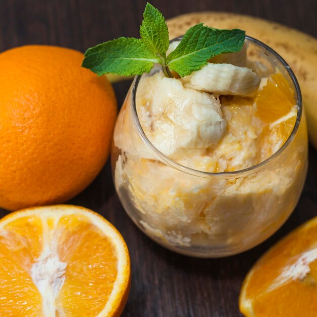 Fruits bananes et oranges à la menthe en verre avec des fruits entiers sur table en bois