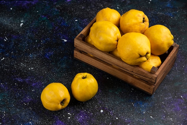 Fruits de coing entiers mûrs dans une boîte en bois sur une table sombre.