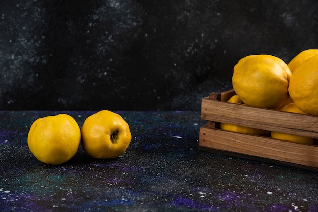 Fruits de coing entiers mûrs dans une boîte en bois sur une table sombre.