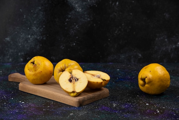 Fruits de coing frais tranchés et entiers sur planche de bois.