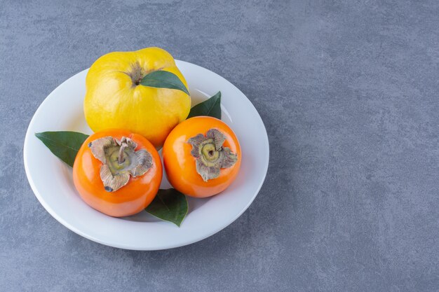 Fruits de coing et de kaki sur la plaque sur la surface sombre