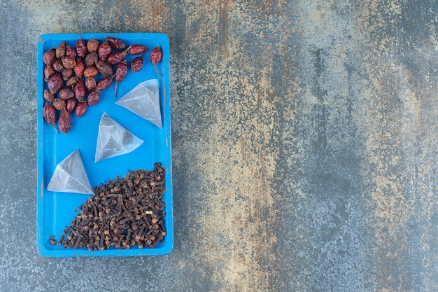 Photo gratuite fruits d'églantier séchés et sachets de thé sur plaque bleue.