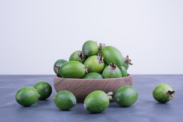 Fruits de feijoa verts dans une tasse en bois sur une table bleue.