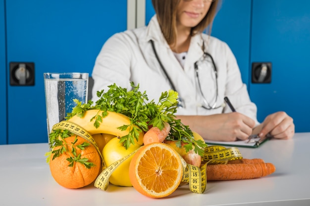 Photo gratuite fruits frais avec ruban à mesurer devant une femme diététicienne écrivant sur presse-papiers