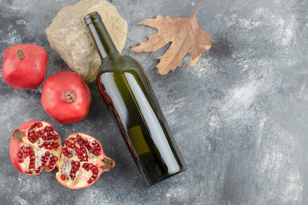 Fruits de grenade mûrs avec une bouteille de vin sur fond de marbre.