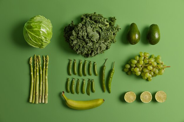 Photo gratuite fruits et légumes crus sains verts. chou frais récolté, citron vert, avocat, asperges, pois, raisin, piment et banane isolés sur fond vif. ensemble de produits naturels biologiques.