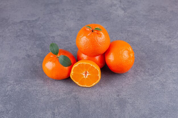 Fruits de mandarine entiers et tranchés avec des feuilles placées sur une table en pierre.