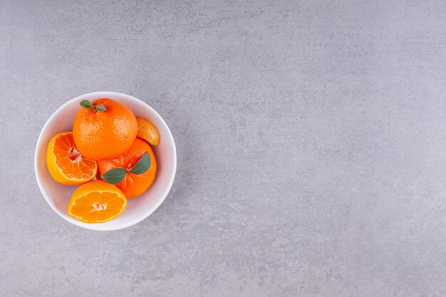 Fruits orange entiers avec des feuilles vertes placées sur une assiette blanche.