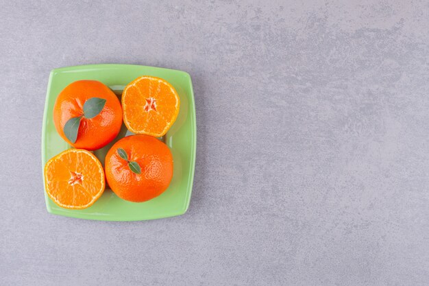 Fruits orange entiers avec des mandarines tranchées placés sur une assiette verte.