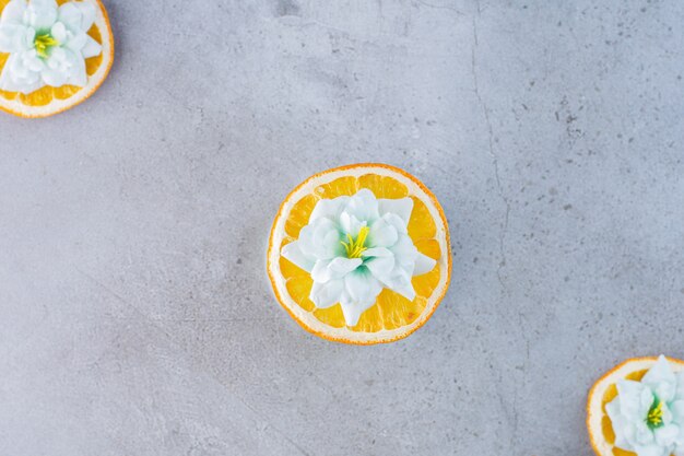 Fruits orange tranchés avec des fleurs blanches sur fond gris