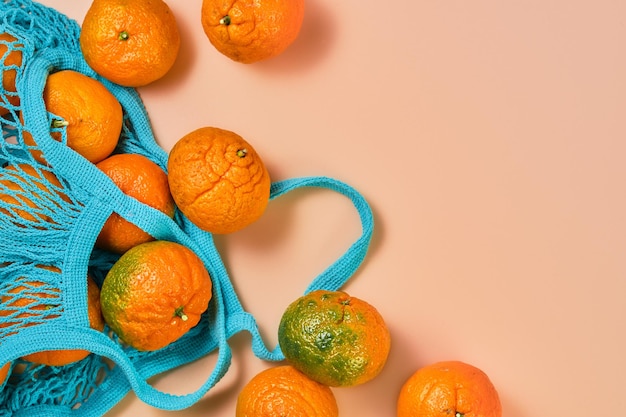 Fruits oranges mandarines ou mandarines sur table de corail. mandarines éparpillées sur la table à partir d'une pochette bleue. mise à plat et espace de copie