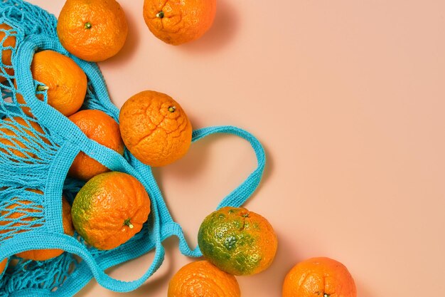 Fruits oranges mandarines ou mandarines sur table de corail. Mandarines éparpillées sur la table à partir d'une pochette bleue. Mise à plat et espace de copie