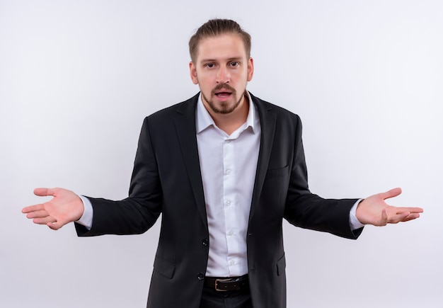 Frustré bel homme d'affaires portant costume regardant la caméra confus debout sur fond blanc