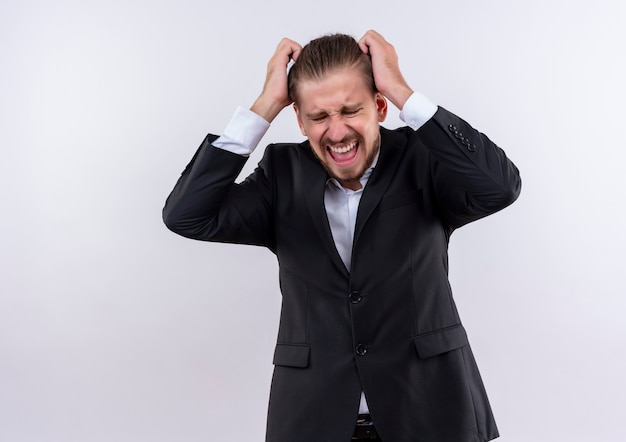 Frustré bel homme d'affaires portant costume se déchaînant en tirant ses cheveux debout sur fond blanc