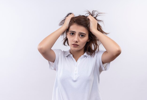 Frustré jeune fille aux cheveux courts portant un polo blanc tirant ses cheveux