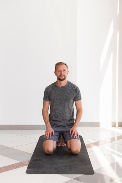 Full shot homme assis sur un tapis de yoga