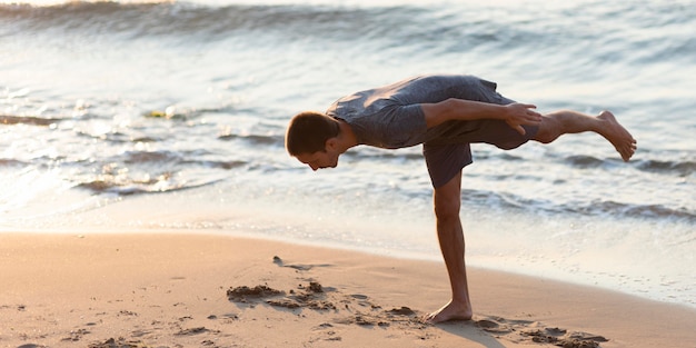Photo gratuite full shot homme pratiquant le yoga avec la mer derrière