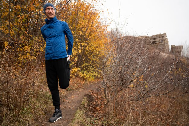 Full shot man stretchig ses jambes en forêt