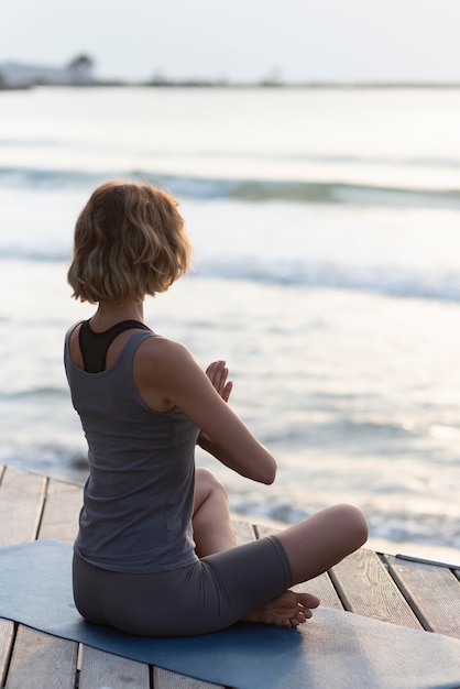 Photo gratuite full shot woman doing sukhasana sur tapis face à la mer