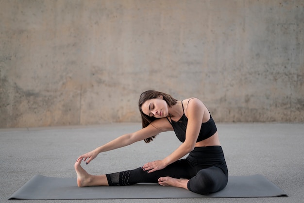 Full shot woman stretching jambe sur tapis