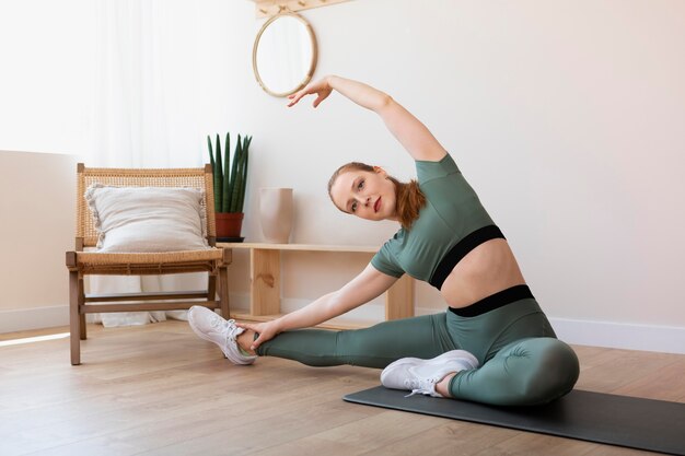 Full shot woman stretching sur tapis à l'intérieur